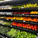 A black perforated metal shelf with piles of red, orange, and red bell peppers on it.