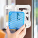 A hand holding a blue plastic cover with a blue and white hexagonal grid inside.