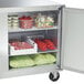 A Traulsen undercounter refrigerator with food inside including tomatoes in a plastic container.