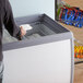 An Avantco glass top display ice cream freezer with a person putting a bag of food inside.