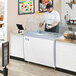 A man in a white shirt and black cap working at an Avantco ice cream dipping cabinet.