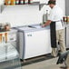 A man in a white apron standing in front of an Avantco ice cream dipping cabinet.