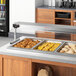 A ServIt Sneeze Guard set on a counter with food trays.