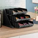 A black plastic Cambro storage rack with 3 black condiment bins on a counter.