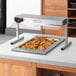 A tray of fried chicken under a ServIt Sneeze Guard on a counter.