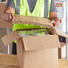 A person in a safety vest opening a white paper fiber box.