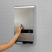 A stainless steel, surface-mounted, no-touch sanitary napkin and tampon dispenser installed on a tiled wall.