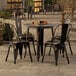 A Lancaster Table & Seating outdoor table in distressed copper with four black chairs on an outdoor patio.