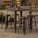 A Lancaster Table & Seating bar height outdoor table with four barstools on a patio.