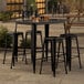 A Lancaster Table & Seating black bar table with four backless barstools on a patio.