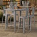 A Lancaster Table & Seating outdoor bar height table with four chairs on a patio.