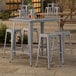 A Lancaster Table & Seating nickel gray bar height table with four backless barstools outside.