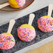 A Coco Bakery Meyer Lemon macaron on a stick with yellow and pink frosting and sprinkles.