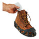 A hand using a white adhesive pad to attach an Ergodyne N-Ferno air-activated toe warmer to a brown boot.