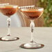 Two Bormioli Rocco America coupe glasses filled with brown liquid and straws.