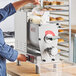 A woman using a Estella countertop pasta extruder machine to pour liquid into it.