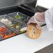 A person using a Traulsen sandwich prep table to cut a bagel.