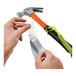 A person's hands using a grey Ergodyne tool tether to attach a tape to a hammer.