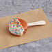 A Coco Bakery chocolate macaron pop with white frosting and sprinkles.