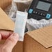 A hand holding a Clariant Sorb-It silica desiccant packet in a box.