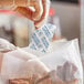 A person in a plastic glove putting a Clariant Oxy-Guard oxygen absorber packet in a bag of meat.