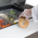 A hand in a glove putting a bagel into a food tray on a Traulsen sandwich prep table.