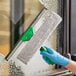 A person wearing a blue glove using a Unger VisaVersa Pro window squeegee with a green handle to clean a window.