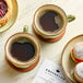 A table with coffee cups and pastries on plates, a sandwich on a plate, and a cup of coffee on a coaster.