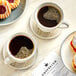 A group of coffee cups and pastries on a table with a white plate.