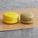 Two yellow macarons with brown filling on a brown surface.