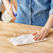 A woman using a Tork white light-duty wiper to clean a table.