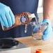 A person in blue gloves pouring Bar Keepers Friend coffee maker cleaner into a measuring cup.