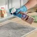 A person in blue gloves spraying Bar Keepers Friend Granite & Stone Cleaner on a counter.