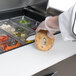 A person in gloves cutting a bagel over a counter with food in plastic containers.