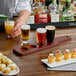 An Acopa mahogany flight paddle holding glasses of beer and appetizers.