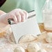 A person using a Choice stainless steel dough cutter to cut dough on a table.