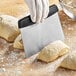 A person using a Choice stainless steel dough cutter to cut dough on a wooden surface.