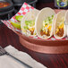 A round paprika deli server filled with tacos, lettuce, and cheese on a table.