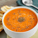 A bowl of orange soup with McCormick basil leaves on top next to a spoon and toast.