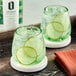 A pair of glasses with Optimist Botanicals non-alcoholic spirit and lime slices on a table.