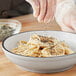 A person sprinkling McCormick Coarse Ground Black Pepper on a bowl of spaghetti.