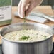 A person's gloved hand sprinkling McCormick Culinary Parsley Flakes into a pot of food.