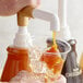 A person pouring Torani Caramel Flavoring Sauce into a cup of ice.