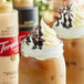 Two glass jars of coffee with whipped cream, one with Torani Dark Chocolate Sauce on top.