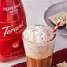 A glass of coffee with Torani Puremade Peppermint Bark Flavoring Sauce and a red and white striped straw.