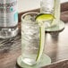 A bottle of Monin Hydration Boost Syrup on a table with a glass of water with ice and lime wedges.