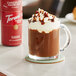 A glass cup of Torani Chocolate Hazelnut flavored hot chocolate with whipped cream and chocolate syrup.