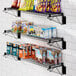 A Regency black epoxy wall-mount wire shelf with snacks and drinks on it.
