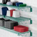 A Regency green metal wire shelf holding dishes, plates, and cups.