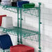 A green wire shelf with white containers and red mats on it.